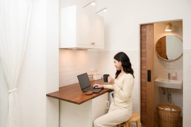 Evde, yaşam tarzında ve tele çalışma konseptinde çalışan Asyalı genç bir kadın dizüstü bilgisayar kullanıyor.