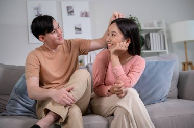 Happy young Asian couple sitting on sofa relaxing together in living room at home