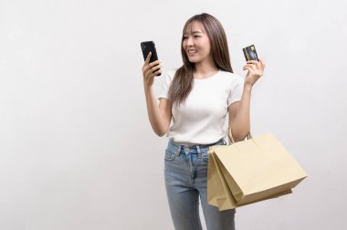 A Young asian woman holding shopping bag and credit card over white background studio, shopping and finance concept.