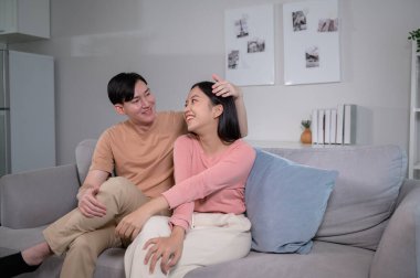 Happy young Asian couple sitting on sofa relaxing together in living room at home