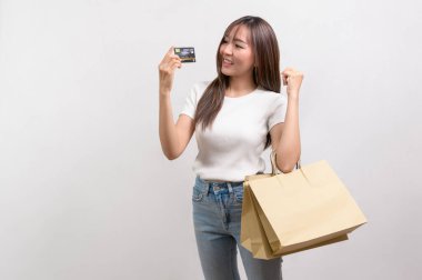 A Young asian woman holding shopping bag and credit card over white background studio, shopping and finance concept.