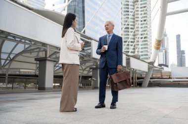 Asian senior mature middle aged businessman and young businesswoman having a discussion and coffee in modern city
