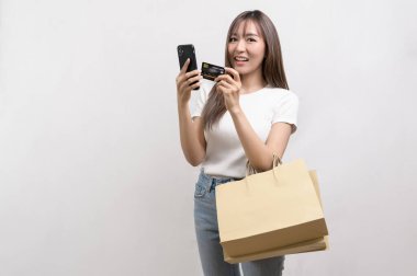 A Young asian woman holding shopping bag and credit card over white background studio, shopping and finance concept.