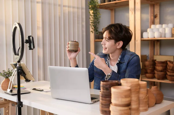 stock image A young Asian man entrepreneur live streaming to sale craft products  to customers in his shop , Technology online business concept.