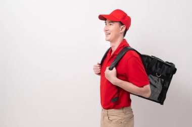 Kırmızı üniformalı Asyalı genç yemek teslimatçısı beyaz arka planda gülen yiyecek çantası taşıyor. 