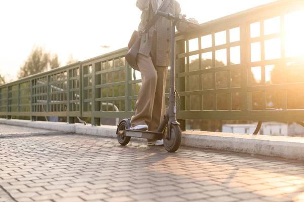 Modern şehir arka planında köprü üzerinde çalışmak için elektrikli scooterlı genç bir iş kadınının portresi.