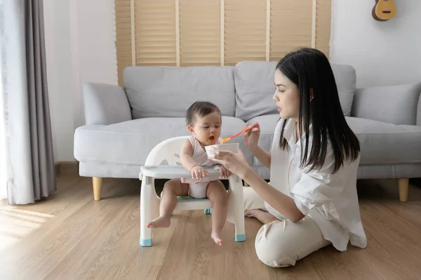 A Young mother helping baby eating blend food on baby chair