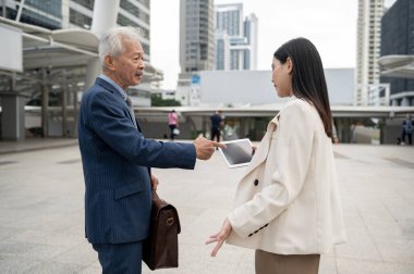 Asyalı yaşlı orta yaşlı işadamı ve genç iş kadını modern şehirde tartışıyorlar.