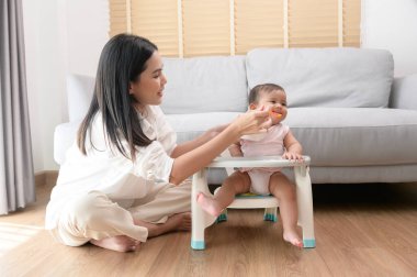 Genç bir anne bebek koltuğunda bebek maması yemesine yardım ediyor.