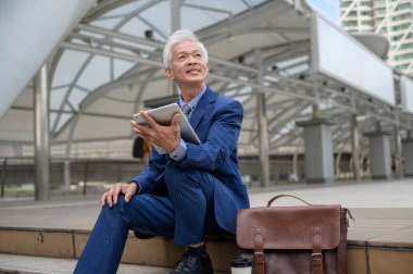 Asyalı yaşlı orta yaşlı işadamı modern şehirde tablet kullanıyor.