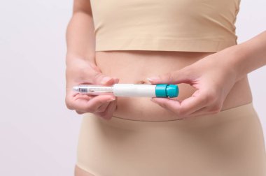 Close up woman using IVF treatment injection on belly to prepare reproductive fertility , Ovulation stimulation .	