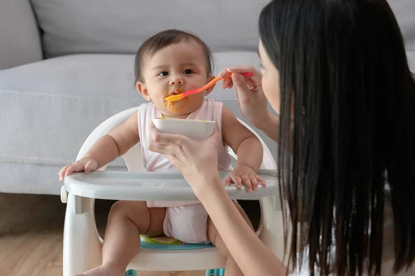 A Young mother helping baby eating blend food on baby chair