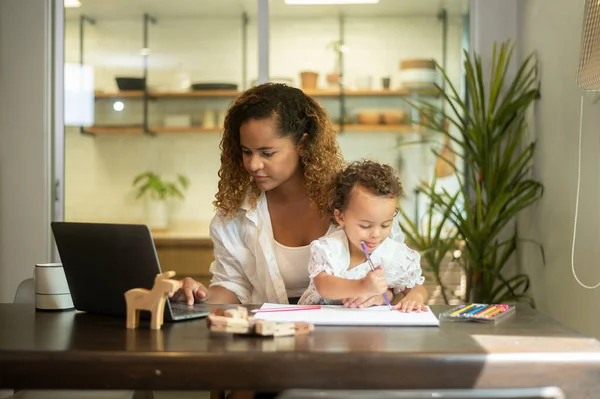 stock image African American mother wearing casual clothes working in her home while daughter playing  or education 