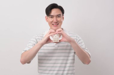 Küçük model evi beyaz arka plan stüdyosunun üzerinde tutan genç adam.