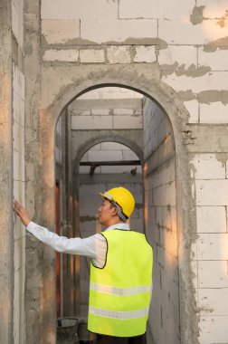 Güvenlik kaskı takan Asyalı bir mühendis inşaat alanını kontrol ediyor ve projenin ilerlemesini inceliyor. 