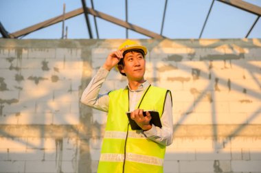 Asyalı bir mühendis kafasına koruyucu bir kask takıyor. Tablet Analitik Mühendisliği verilerini kullanıyor.