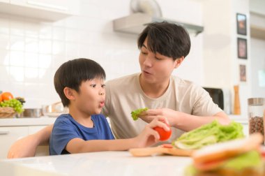 Mutlu Asyalı baba ve oğul evde sağlıklı yiyecekler yiyorlar. 