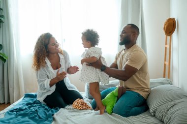 Mutlu Afrikalı Amerikalı ebeveynler ve küçük kızları evdeki yatak odasında oynuyorlar. Mutlu aile kavramı.