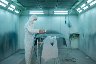 Kafkasyalı adam tamirhanede boya tabancası kullanıyor.