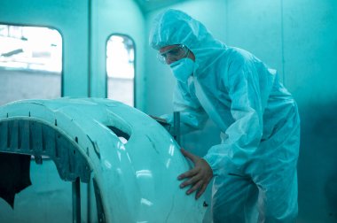 Beyaz adam tamirci dükkanında boya sıkmadan önce araba parçalarını temizliyor.