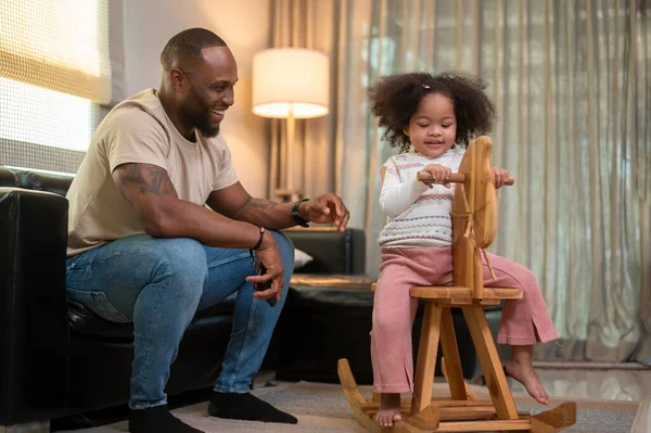 Happy African American man playing with his daughter in living room at home