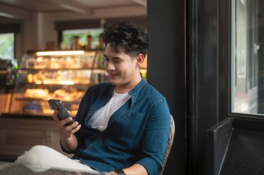 Genç Asyalı adam kafede akıllı telefon kullanıyor.