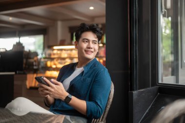 Genç Asyalı adam kafede akıllı telefon kullanıyor.