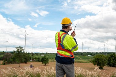 Kafasında koruyucu miğfer olan akıllı bir mühendis, elektrik türbinleri alanında telsiz kullanıyor.