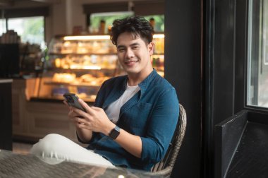 Genç Asyalı adam kafede akıllı telefon kullanıyor.