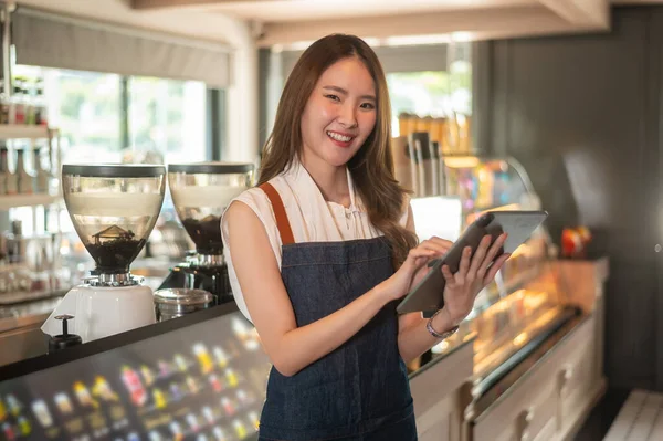 An Asian woman entrepreneur using tablet checking stock or sale income in modern coffee shop , concept small business