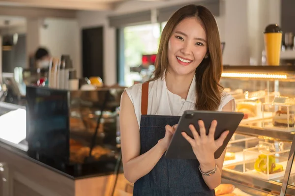 An Asian woman entrepreneur using tablet checking stock or sale income in modern coffee shop , concept small business