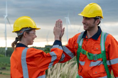  Koruyucu kasklı akıllı mühendisler elektrik türbinleri alanında neşeyle beşlik çakıyor.