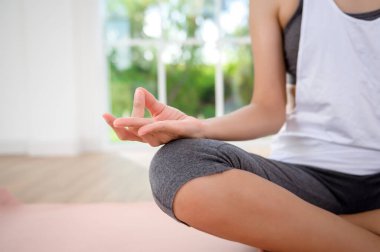 Spor giyimli genç bir kadın meditasyon yapıyor ve yoga yapıyor. Kapalı alanda, sağlıklı yaşam tarzı, zihinsel sağlık konsepti..