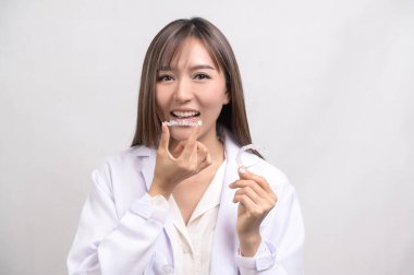 A Young female dentist holding invisalign braces over white background studio, dental healthcare and Orthodontic concept. clipart