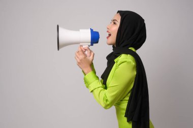 A Young muslim woman with hijab holding megaphone over white background studio.	