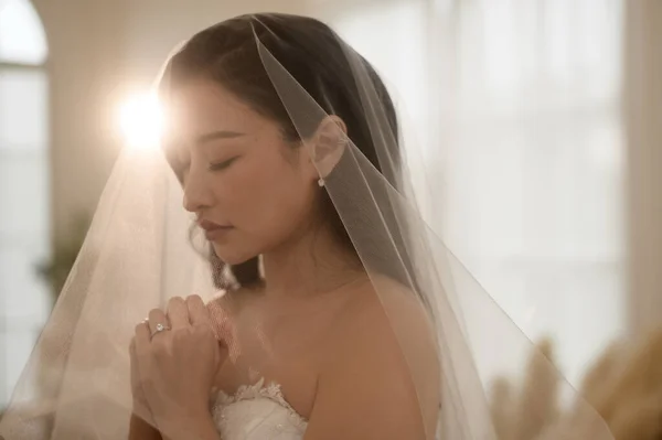 Stock image Beautiful bride in wedding dress covered by white veil, folding her arms and praying on ceremony, Love and marriage concept