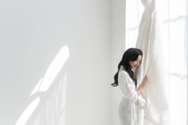 Beyaz banyolu gelin düğün gününe hazırlanan zarif gelinliğe dokunuyor ve hayran kalıyor. Aşk ve evlilik kavramı.