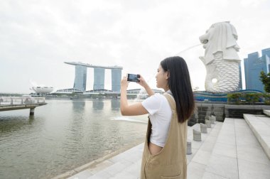 SINGAPORE - 28 / 12 / 2022: Marina Körfezi Sands Oteli önünde genç Asyalı kadın turistle birlikte Merlion Fountain. 