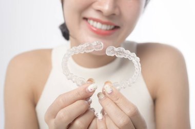 Young smiling woman holding invisalign braces over white background studio, dental healthcare and Orthodontic concept.	