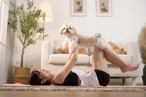 Young woman in sportswear doing meditation practice and yoga with cute dog in living room, healthy lifestyle, Mental health concept.