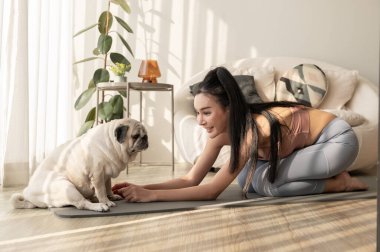 Spor giyinen Asyalı bir kadın evde tatlı bir köpekle yoga yapıyor, sağlıklı bir yaşam tarzı, akıl sağlığı konsepti..