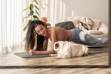 Spor giyinen Asyalı bir kadın evde tatlı bir köpekle yoga yapıyor, sağlıklı bir yaşam tarzı, akıl sağlığı konsepti..