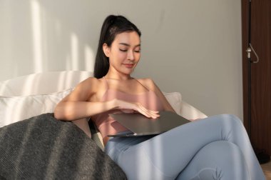 Genç Asyalı kadın evdeki oturma odasında dizüstü bilgisayarla çalışıyor.