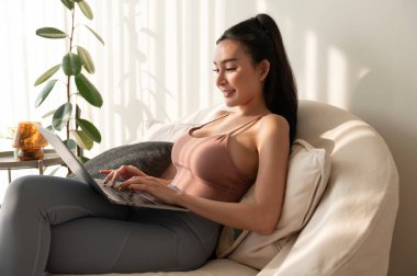 Genç Asyalı kadın evdeki oturma odasında dizüstü bilgisayarla çalışıyor.