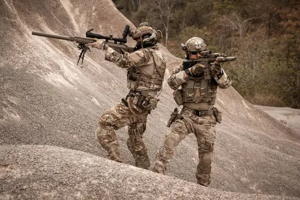 Kamuflaj üniformalı askerler tüfeklerini doğrultuyorlar.