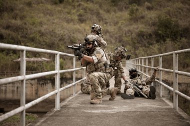 Kamuflaj üniformalı askerler tüfeklerini doğrultuyorlar.