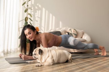 Spor giyinen Asyalı bir kadın evde tatlı bir köpekle yoga yapıyor, sağlıklı bir yaşam tarzı, akıl sağlığı konsepti..