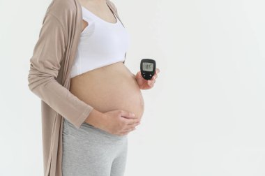 Pregnant woman checking blood sugar level by using Digital Glucose meter, health care, medicine, diabetes, glycemia concept clipart