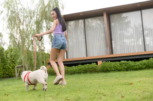 Mutlu Asyalı kadın arka bahçede sevimli akıllı köpek yavrusuyla oynuyor.