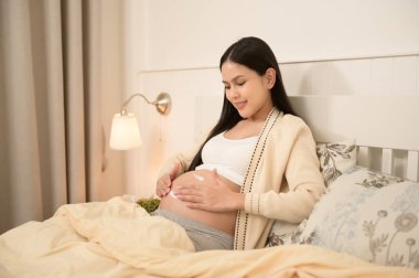Güzel hamile bir kadın nemlendirici sürüyor, göbeğinde gerilme izi kremi, kısırlık tedavisi, tüp bebek, gelecekteki annelik konsepti.